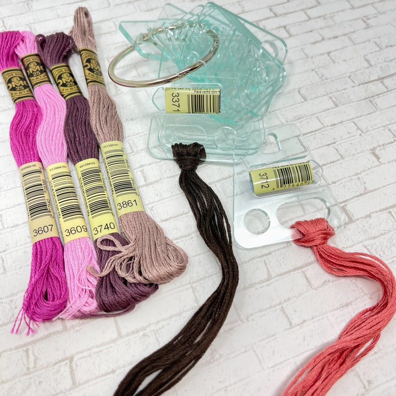 May include: Assortment of embroidery floss spools in pink, purple, brown, and beige colors. The spools are labeled with numbers 3607, 3609, 3740, and 3861. There are also two clear plastic organizers with numbers 3371 and 3712.