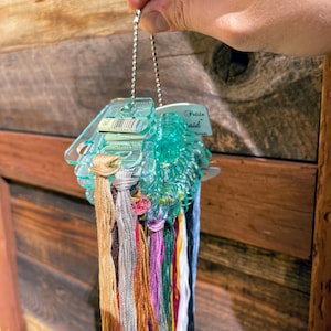 May include: A clear plastic thread organizer with a silver chain. The organizer is filled with colorful embroidery floss. The label on the organizer reads "Petite  Said".