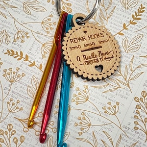 May include: A set of four crochet hooks, attached to a key ring, with a wooden tag that reads "Repair Hooks 3mm-D 4mm-G 5mm-H A Needle Runs Through It". The hooks are yellow, orange, red, and blue.
