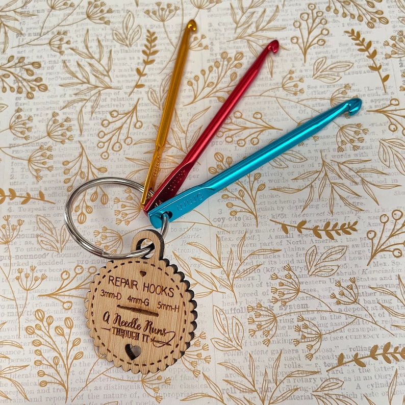 May include: A wooden keychain with a heart-shaped cutout and the text "Repair Hooks 3mm-D 4mm-G 5mm-H A Needle Runs Though It"  The keychain has three colorful crochet hooks attached to it.
