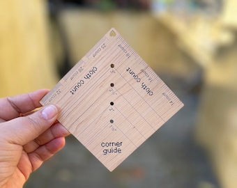 May include: A wooden corner guide tool with markings for 14, 16, 18, 25, 28, and 32 count fabric. The tool has holes for marking 1 1/2, 2, 2 1/2, and 3 inches.