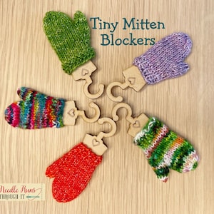 May include: Five colourful knitted mitten-shaped blockers for knitting projects. The blockers are made of wood and have a heart-shaped cutout. The text "Tiny Mitten Blockers" is written above the blockers.