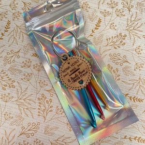 May include: A set of three colorful crochet hooks with a wooden keychain tag that reads "Repair Hooks 3mm-D 4mm-G 5mm-H A Needle Runs Through It".