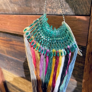 May include: A set of colorful embroidery floss threads organized on a clear plastic organizer with a silver chain. The threads are arranged in a fan shape and are ready for crafting projects.