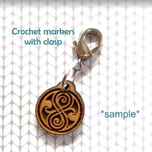 May include: Wooden crochet marker with a silver clasp and a brown, engraved design. The design is a stylized symbol with a swirling pattern. The text "*sample*" is visible in the image.
