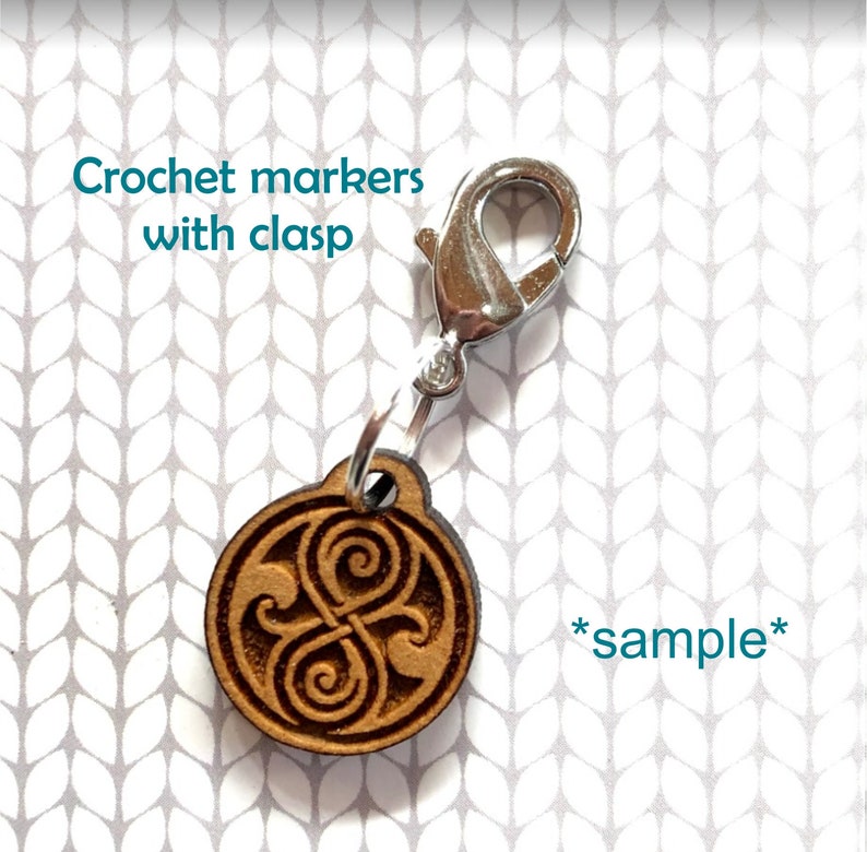May include: Wooden crochet marker with a silver clasp and a brown, engraved design. The design is a stylized symbol with a swirling pattern. The text "*sample*" is visible in the image.