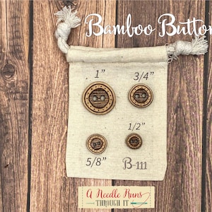 May include: A set of four natural bamboo buttons in a white drawstring bag. The buttons are 1 inch, 3/4 inch, 1/2 inch, and 5/8 inch in diameter. The bag has the text "Bamboo Buttons" and "B-111" printed on it.