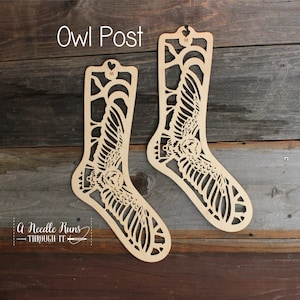 May include: Two wooden sock blockers shaped like owls with wings outstretched. The text "Owl Post" is above the blockers. The text "A Needle Runs Through It" is below the blockers.