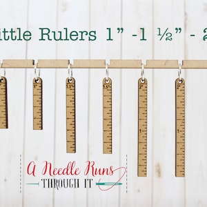 Pode incluir: Seis r&eacute;guas de madeira com an&eacute;is de metal pendurados numa barra de madeira. As r&eacute;guas medem 2,5 cm, 3,8 cm e 5 cm de comprimento. O texto "Little Rulers 1" - 1 1/2" - 2" est&aacute; no topo da imagem. O texto "A Needle Runs THROUGH IT" est&aacute; na parte inferior da imagem.