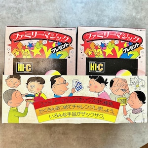 以下が含まれることがあります： カラフルな星柄と日本語で「プレゼント」と書かれた「ファミリーマジック」セットの箱が2つ。箱には「Hi-C」のロゴと子供たちの漫画イラストが描かれています。箱の下部には日本語のテキストがあります。