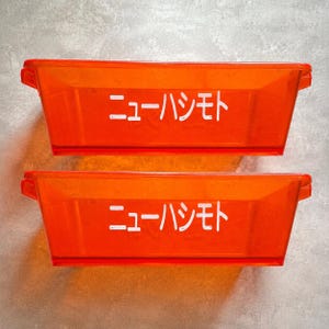 May include: Two rectangular, translucent orange plastic storage bins with integrated side handles. Each bin features the white Japanese text "ニューハシモト" printed clearly on the front center, showcasing a simple, functional design.