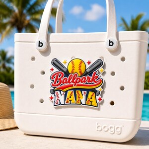 May include: White tote bag featuring a baseball design. The graphic shows a yellow baseball, crossed bats, and the words "Ballpark NANA" in red, yellow, and blue. The bag has white handles and the brand name "bogg" is visible.