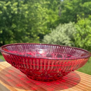 May include: A vibrant red glass bowl featuring a textured diamond pattern on the exterior and vertical ribbing along the upper rim. The bowl has a wide, shallow circular shape with a translucent finish that catches the light, creating a deep crimson hue.