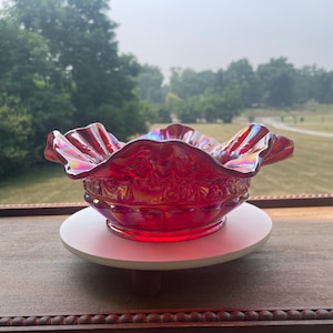 Peut inclure: Un bol en verre carnaval rouge vif doté d'une finition irisée et d'un bord festonné et ondulé. L'extérieur du bol présente un motif floral en relief détaillé avec une base circulaire, reflétant la lumière avec des reflets multicolores.