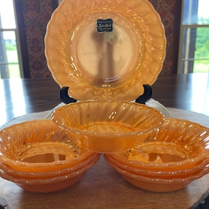 Könnte beinhalten: Ein Set aus fünf pfirsichfarbenen, irisierenden Glasschalen mit gewelltem Rand und einem passenden Teller mit dem Etikett Lustre Shell Heat Resistant. Das Glasgeschirr hat eine gerippte Textur und eine glänzende Oberfläche, gestapelt angeordnet.