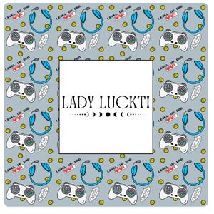 Op de afbeelding: Een lichtblauwe achtergrond met een wit kader. Het kader bevat de tekst "LADY LUCKTI" in zwart. De achtergrond is gevuld met een herhalend patroon van blauwe en witte gamecontrollers, blauwe koptelefoons en gele munten. De tekst "LEVEL UP DAD" en "GG DADD" wordt ook herhaald in het patroon.