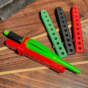 Könnte beinhalten: Ein rot-grünes stiftähnliches Werkzeug mit grüner Spitze und ein schwarzer Stift. Drei weitere Werkzeuge sind in Grün, Schwarz und Rot. Alle Werkzeuge haben eine Reihe von Löchern. Die Artikel befinden sich auf einer Holzoberfläche.