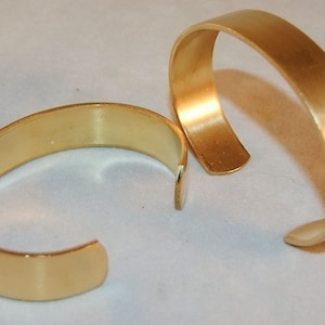 K&ouml;nnte beinhalten: Zwei goldfarbene Metallarmb&auml;nder, eines etwas gr&ouml;&szlig;er als das andere, werden auf einer wei&szlig;en Oberfl&auml;che gezeigt. Die Armb&auml;nder sind schlicht und haben eine glatte, polierte Oberfl&auml;che.
