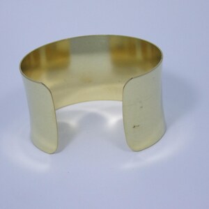 May include: A gold-coloured metal cuff bracelet with a simple, rounded design.