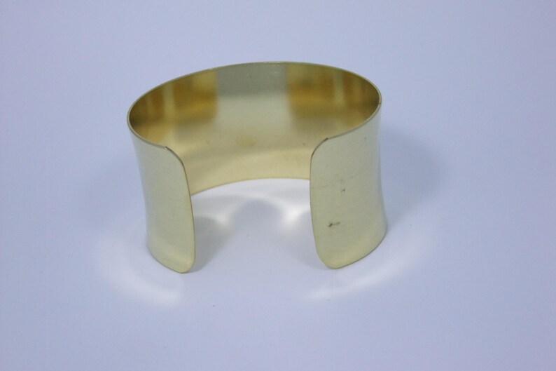 May include: A gold-coloured metal cuff bracelet with a simple, rounded design.