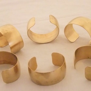 May include: Six gold metal napkin rings. The rings are simple and have a smooth, polished finish.