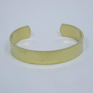 Puede incluir: Una pulsera simple de metal dorado con una superficie lisa y plana.