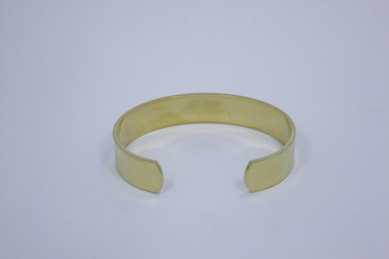 K&ouml;nnte beinhalten: Ein schlichtes, goldfarbenes Metall-Armreif-Armband. Das Armband ist an beiden Enden offen und hat eine glatte, polierte Oberfl&auml;che.