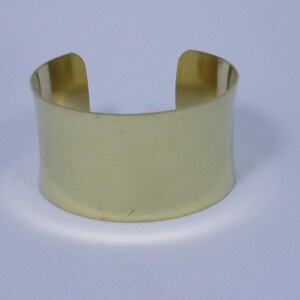 May include: A gold-coloured metal cuff bracelet. The bracelet is simple and has a smooth, polished finish.