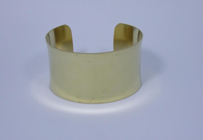 May include: A gold-coloured metal cuff bracelet. The bracelet is simple and has a smooth, polished finish.