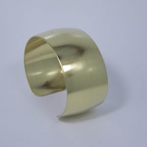 May include: A gold-toned metal cuff bracelet with a smooth, polished finish.