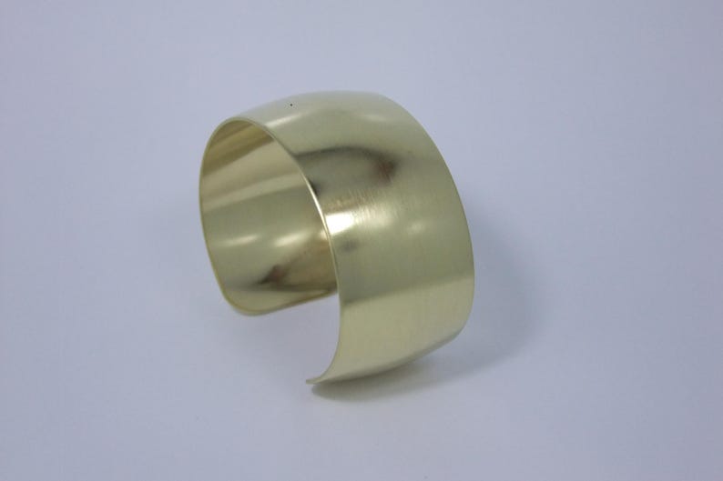 May include: A gold-toned metal cuff bracelet with a smooth, polished finish.