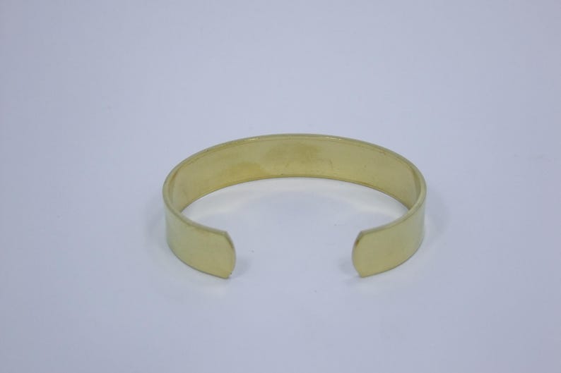 Puede incluir: Un brazalete simple de metal de color dorado. El brazalete est&aacute; abierto en ambos extremos y tiene un acabado liso y pulido.
