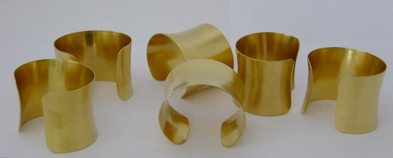 May include: Six gold-coloured metal bracelets with a curved design. The bracelets are stacked on top of each other.
