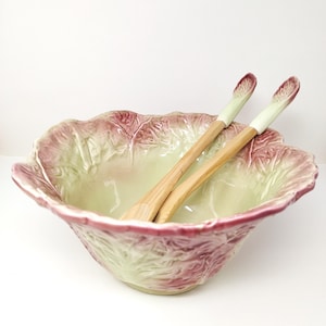 Puede incluir: Un cuenco de cerámica para ensalada con forma de cabeza de radicchio, con bordes ondulados en tonos verde pálido y magenta intenso. Dos cubiertos de ensalada a juego con mangos de madera y puntas de cerámica en forma de hoja descansan dentro.
