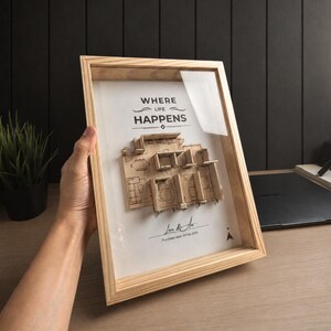 Könnte beinhalten: Ein heller Holzrahmen mit einem 3D-Grundrissmodell aus Holz. Auf dem weißen Hintergrund steht der Text WHERE LIFE HAPPENS, eine Unterschrift und der Text Purchase date: 23 Feb 2026. Ein kleiner schwarzer Richtungspfeil befindet sich in der Ecke.