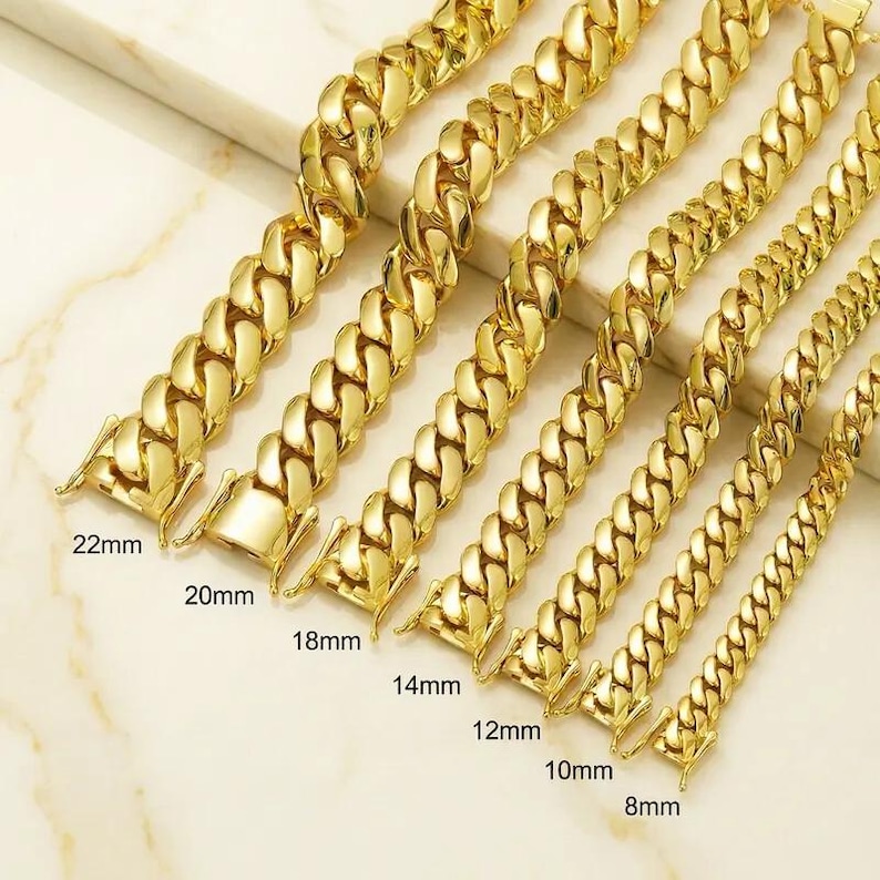 May include: Gold-colored chain necklaces in various widths, from 8mm to 22mm, displayed on a light-colored surface. Each chain features a classic curb link design and a secure clasp. The sizes are labeled on the image.