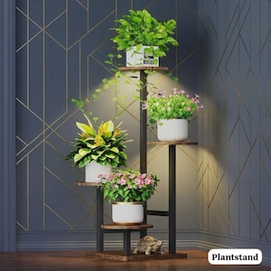 May include: A multi-tiered black metal and wood plant stand featuring five circular shelves arranged at varying heights. The stand holds five potted plants with green foliage and pink or yellow flowers, plus a small turtle figurine on the base.
