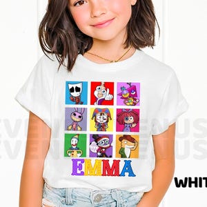 May include: A white short-sleeved t-shirt featuring a grid of nine colorful cartoon character illustrations. Below the grid, the name EMMA is printed in large, multi-colored, polka-dotted letters. The shirt has a crew neckline and a standard fit.