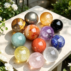 May include: A collection of twelve polished gemstone spheres in various colours and textures, including tiger's eye, pyrite, citrine, black obsidian, amethyst, lapis lazuli, rose quartz, clear quartz, and other smooth, rounded mineral stones.