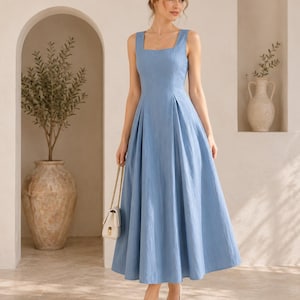 May include: A light blue sleeveless midi dress with a square neckline and a fitted bodice that transitions into a pleated, flared skirt. The dress features a textured fabric and is paired with a small white handbag and white pointed-toe heels.