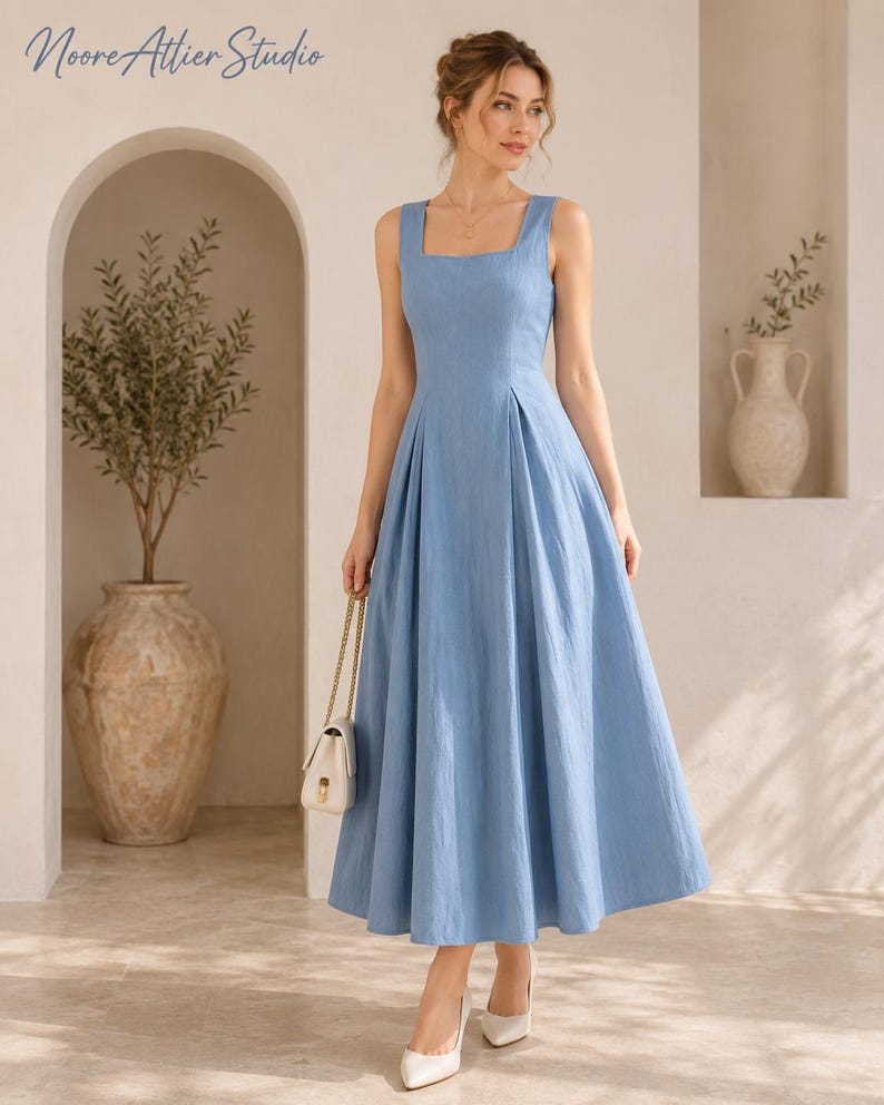 May include: A light blue sleeveless midi dress with a square neckline and a fitted bodice that transitions into a pleated, flared skirt. The dress features a textured fabric and is paired with a small white handbag and white pointed-toe heels.