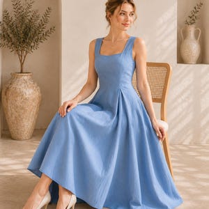 May include: A sleeveless cornflower blue midi dress with a square neckline, a fitted bodice, and a pleated skirt that flares out from the waist. The dress features a solid color and a textured fabric finish, paired with pointed-toe beige heels.