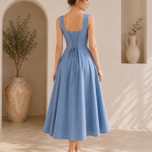 May include: A cornflower blue midi dress featuring a square neckline, wide shoulder straps, and a lace-up corset-style back closure with a long tie. The dress has a fitted bodice and a full, flared skirt that falls below the knee.