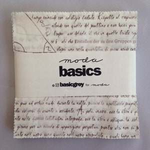 Peut inclure: Une étiquette en tissu blanc avec du texte brun qui dit "moda basics @basicgrey for moda". L'étiquette est pliée et a une surface rugueuse et texturée.