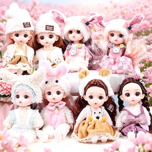 May include: A collection of eight adorable dolls, each with detailed facial features and long hair. The dolls wear various outfits, including dresses and furry hats with animal ears. The hats have the text "Hand made" on them.