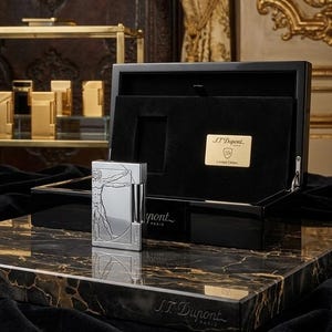Peut inclure: Un briquet rectangulaire argenté orné d'une gravure de l'Homme de Vitruve, présenté avec un coffret laqué noir portant une plaque dorée S.T. Dupont Limited Edition et le logo S.T. Dupont Paris gravé sur la base.