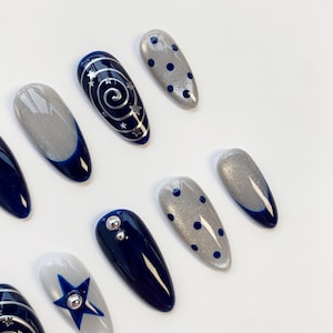 May include: A set of almond-shaped press-on nails featuring a dark navy blue and shimmering silver color palette. Designs include silver spiral and star patterns, dark blue polka dots on silver glitter, solid navy blue, and a blue star accent.