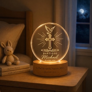 Op de afbeelding: Een rond acryl nachtlampje met een gravure van een kruis en duif, verlicht vanuit een houten voet. De tekst luidt BAPTIZED Michael 20 APRIL 2026, met de inscriptie Called by name, you are Mine. ISAIAH 43:1 op de houten standaard.