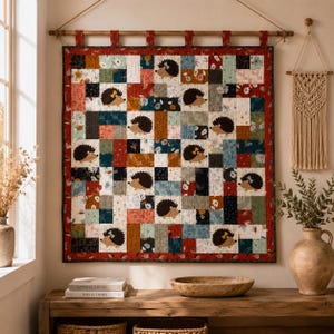 May include: A square patchwork wall hanging quilt featuring a repeating pattern of brown hedgehogs on a background of multi-colored fabric squares in shades of red, blue, green, and white, suspended from a wooden rod with fabric loops.