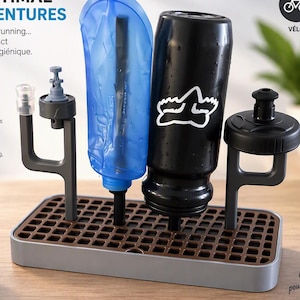 Puede incluir: Un escurridor rectangular gris y marrón con superficie de rejilla, que cuenta con dos soportes verticales grises que sostienen una bolsa de hidratación azul y una botella de agua negra boca abajo, con texto en francés e iconos al lado.